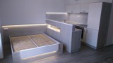 Moderní kuchyň do apartmánu s navázáním na postel. Vhodně zvolené osvětlení dodává celému kompletu luxusní vzhled.